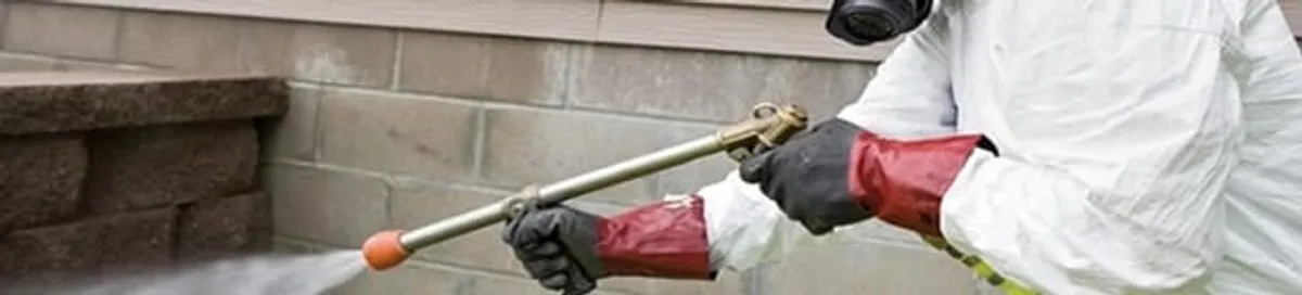 Pest control technician applying exterior insect treatment along a home foundation in Lincoln, NE