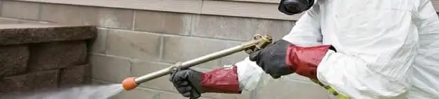 Pest control technician applying exterior insect treatment along a home foundation in Lincoln, NE