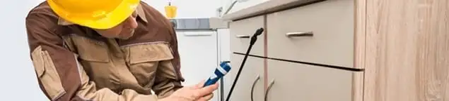 Roach exterminator applying treatment under kitchen cabinets in Lincoln, NE