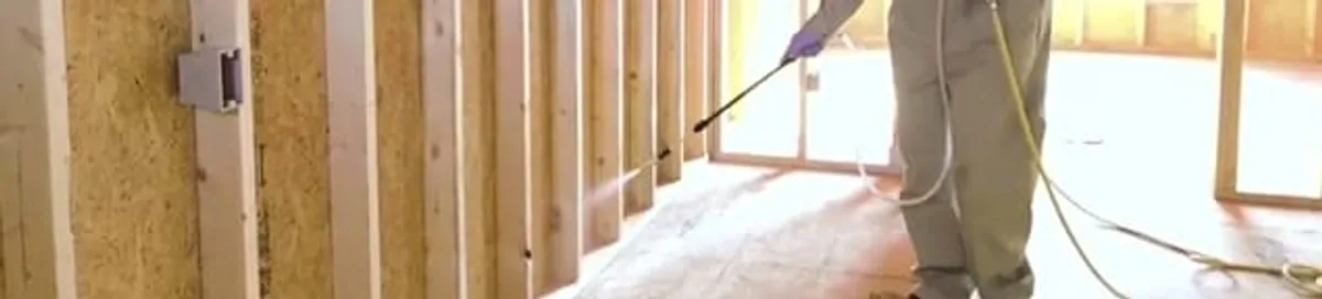 Termite treatment technician applying spray along framing and unfinished walls in Lincoln, NE