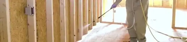 Termite treatment technician applying spray along framing and unfinished walls in Lincoln, NE